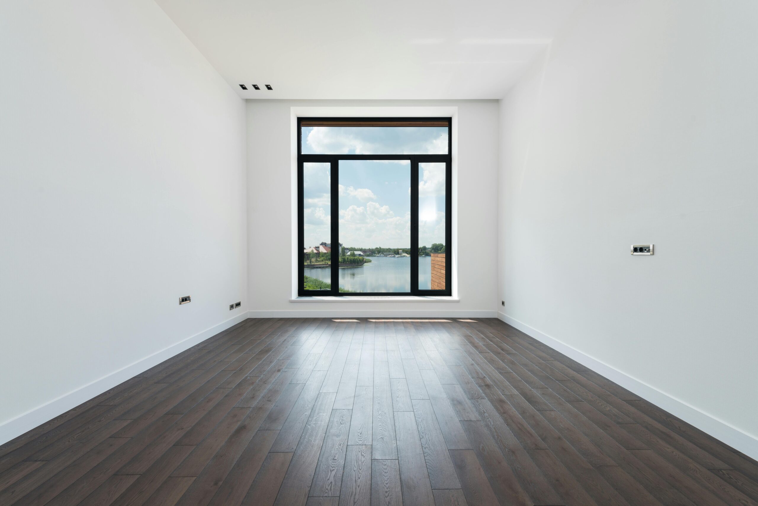 Interior de una habitación moderna, espaciosa y luminosa con suelo de laminado de madera, paredes blancas y ventanas panorámicas