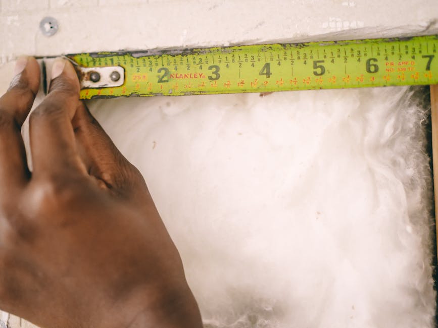 Primer plano de una mano midiendo aislamiento con una cinta métrica amarilla